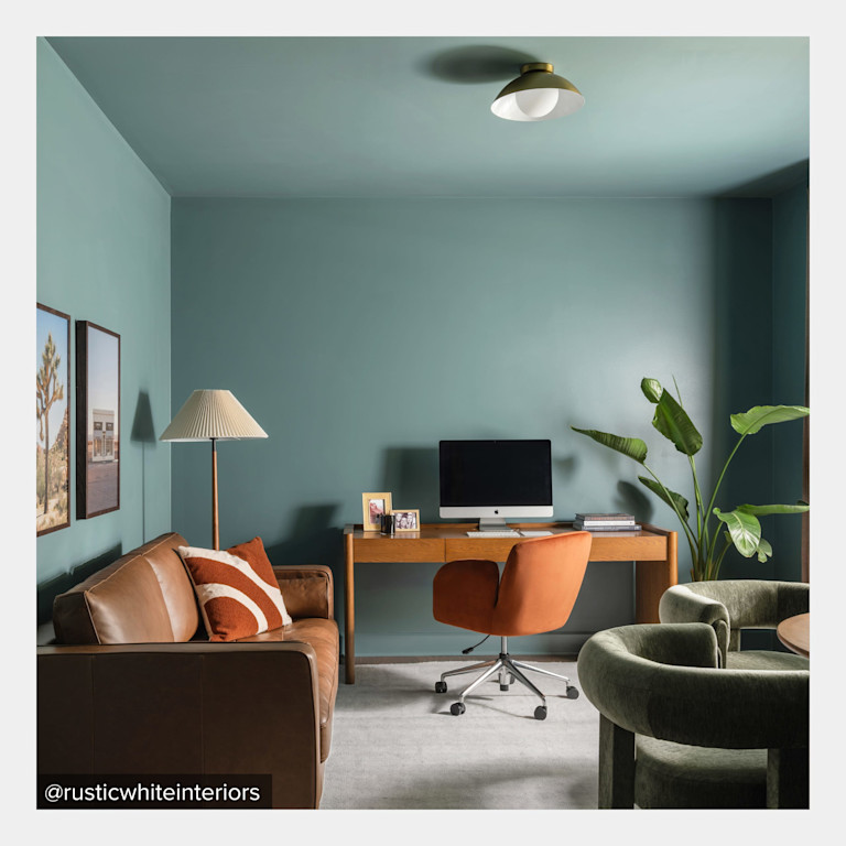 The finished home office, furnished with Article pieces from the design plan: a leather sofa, wood desk, rust-colored office chair, and green lounge chairs against teal walls. Photo by @rusticwhiteinteriors.