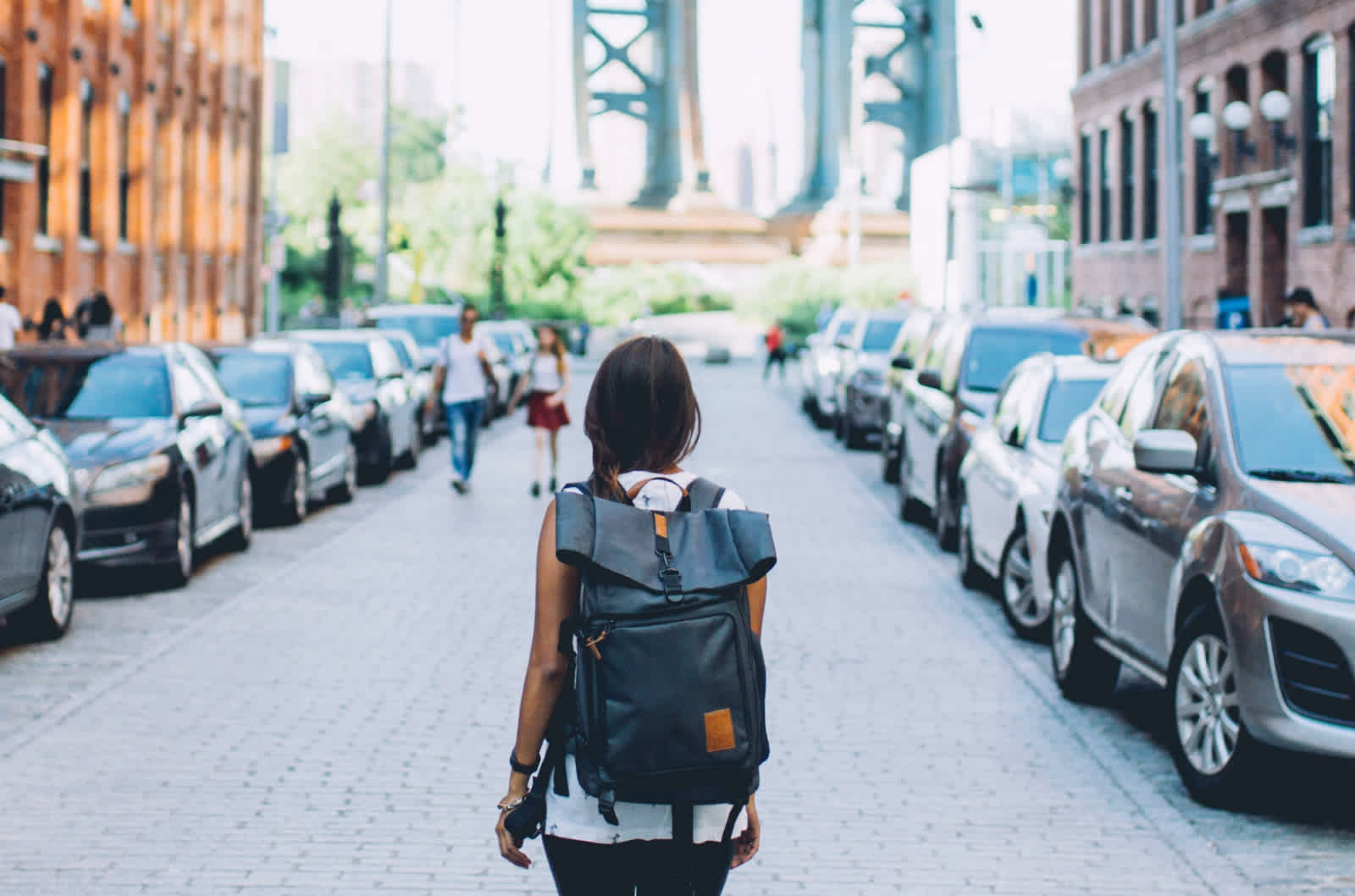 Woman with backpack stands in street with cars parked on both sides