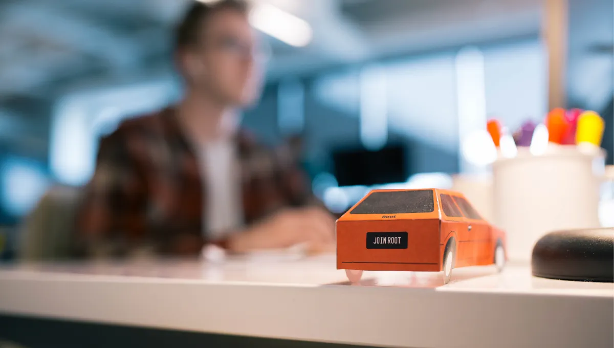 Paper car up close with man working at desk blurred in background