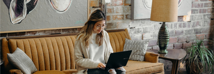 Woman sitting on couch in apartment using laptop | Car and renters insurance bundle page