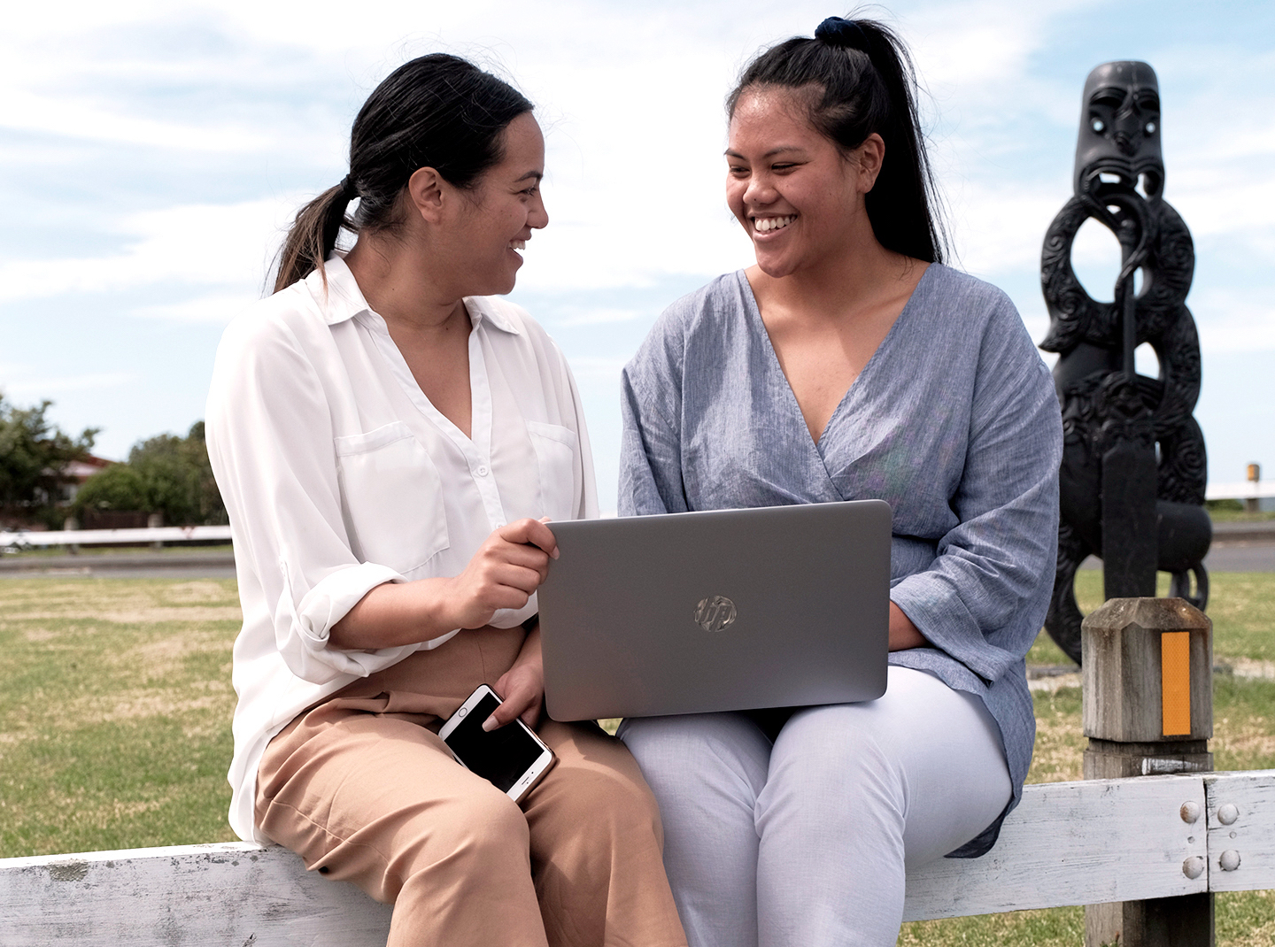 Two Maori women outside holding laptop