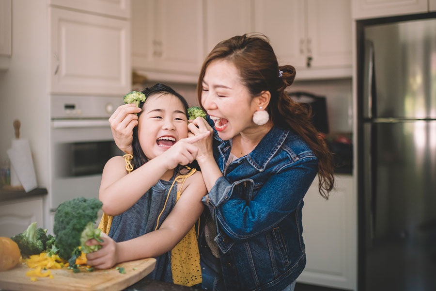 Mother and daughter having fun with broccoli in the kitchen