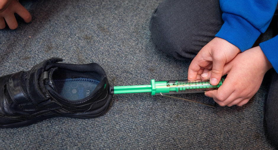 A child measuring the force necessary to push a shoe across the ground.