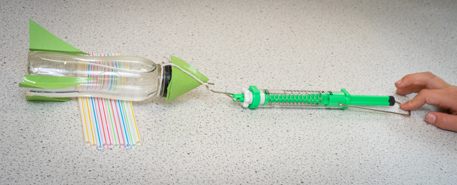 A child measuring the force required to move a bottle rocket using rollers.