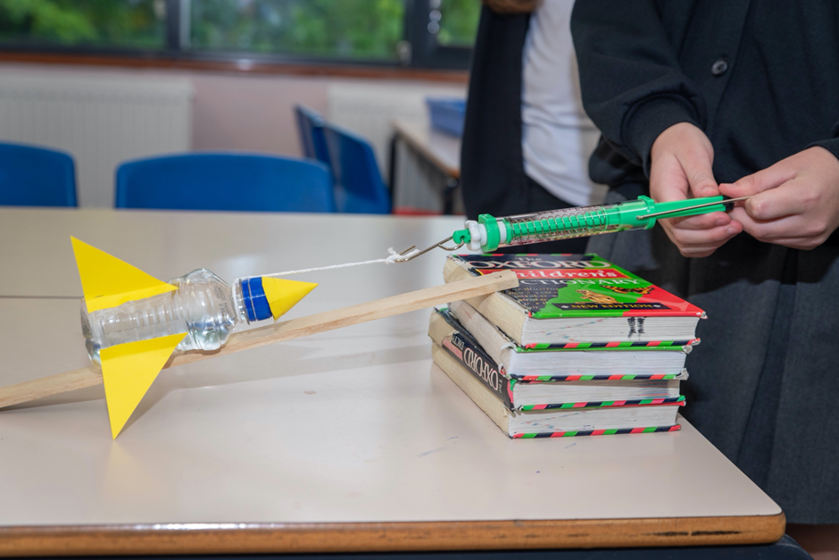A child measuring the force required to move a bottle rocket up an incline.