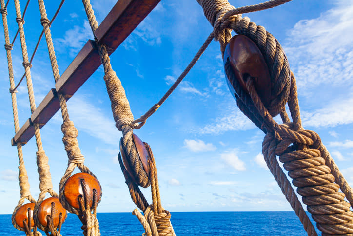 Part of an old sailing wooden ship with a rope ladder with pulleys, knotted ropes and wooden fasteners. Rigging on an old wooden ship against the sea and sky.