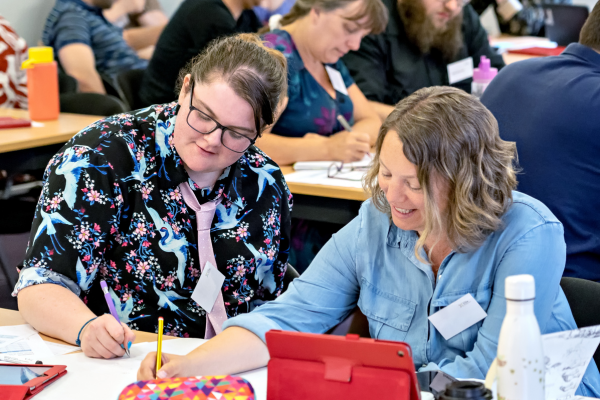 Teachers smiling as they work together to fill in an exercise sheet at a CPD course