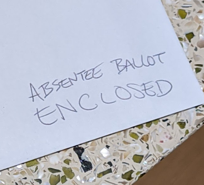An envelope with a handwritten note: "Absentee Ballot Enclosed"