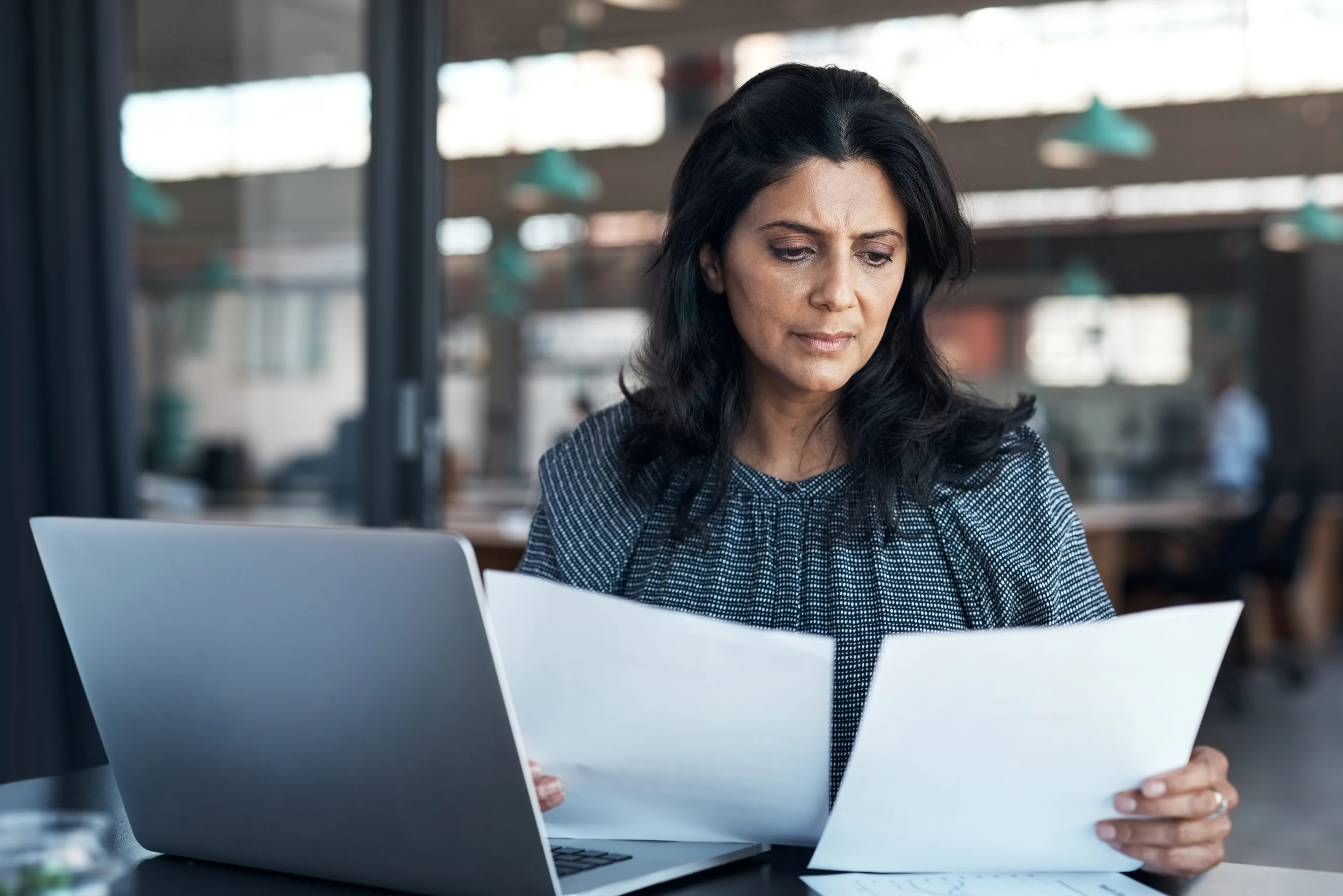 Image - Woman using a laptop and going through paperwork in a modern office