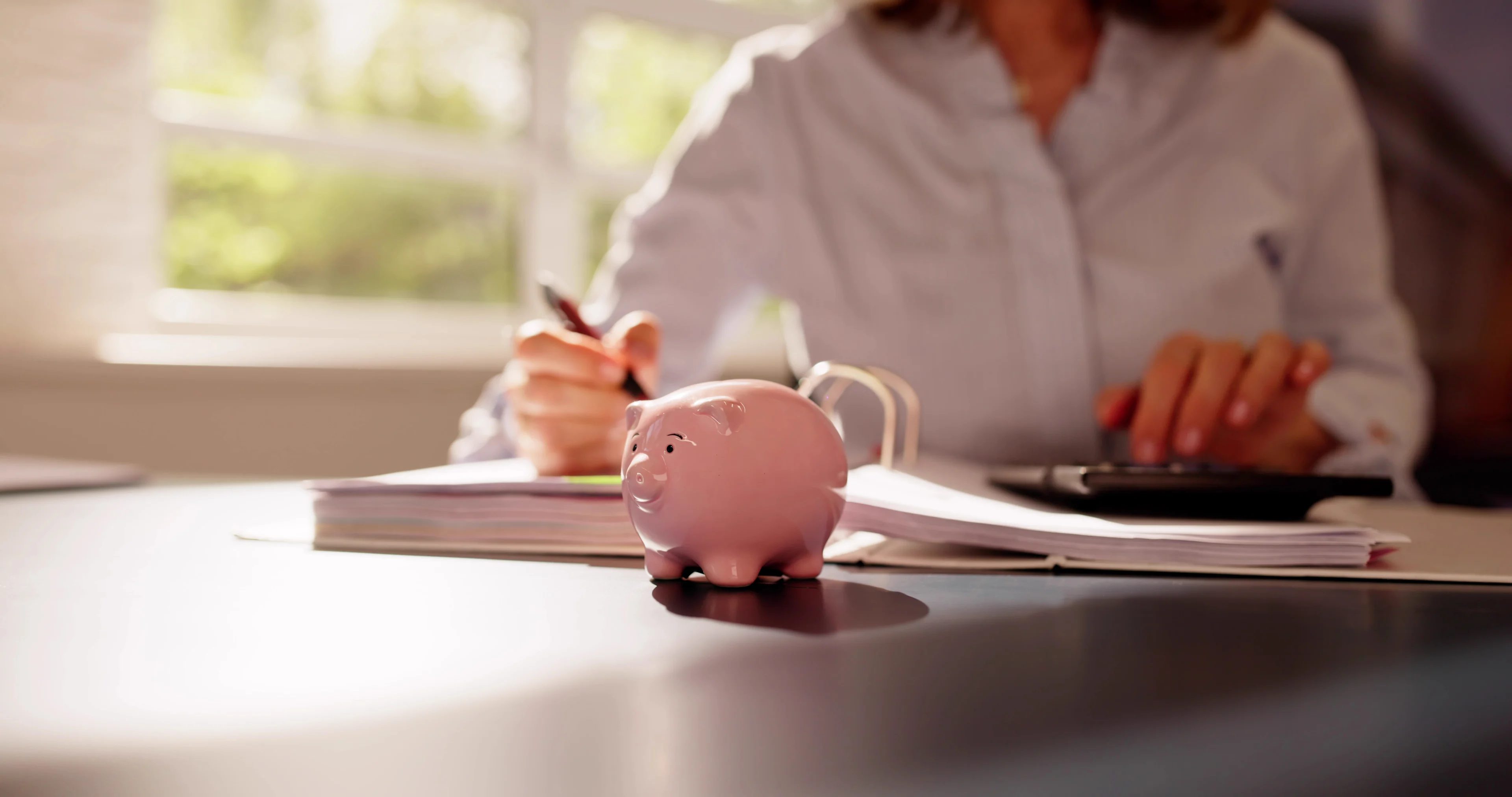 Women sitting with binder, calculator and piggy bank.