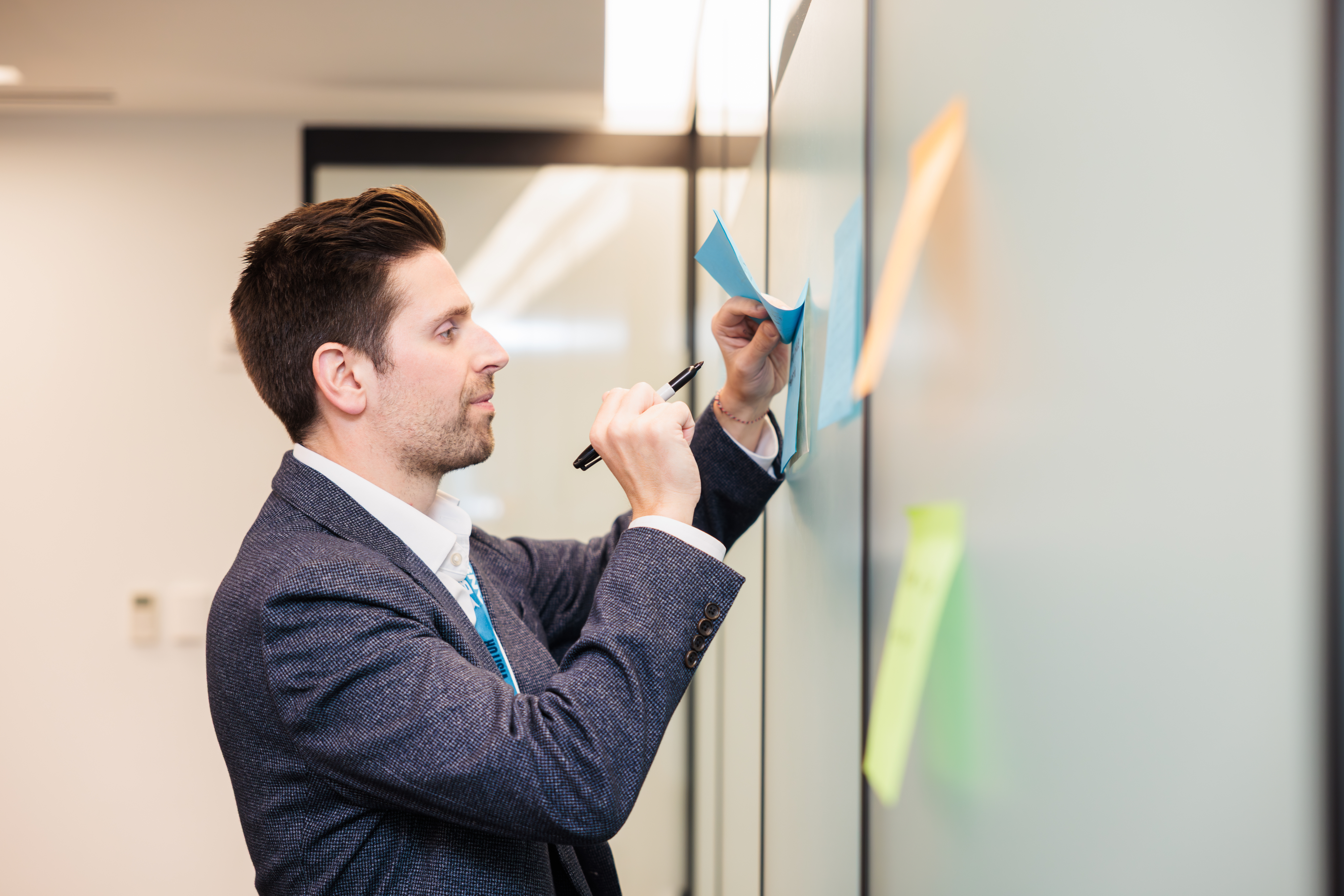 Man at a whiteboard, editing a Post-It! note
