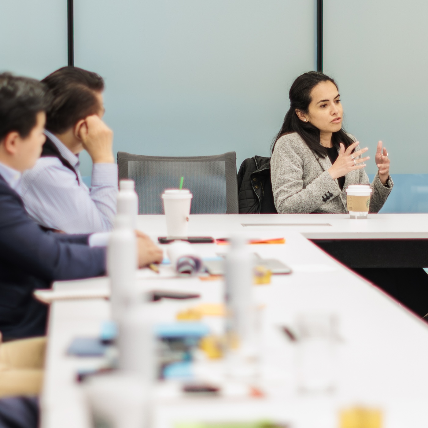 A woman at a conference table, gesturing with her hands as others look on
