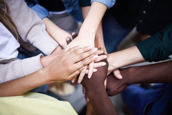 A view from above of a group of hands placed on top of one another in a team huddle.