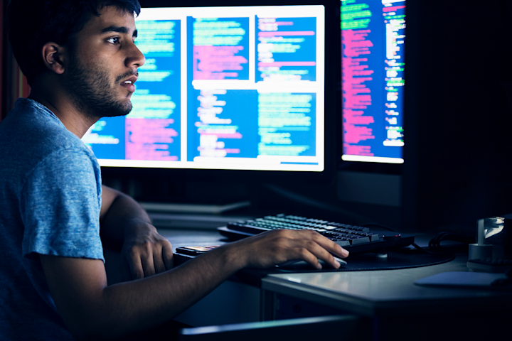 Person sitting at computer and reviewing code on multiple monitors.