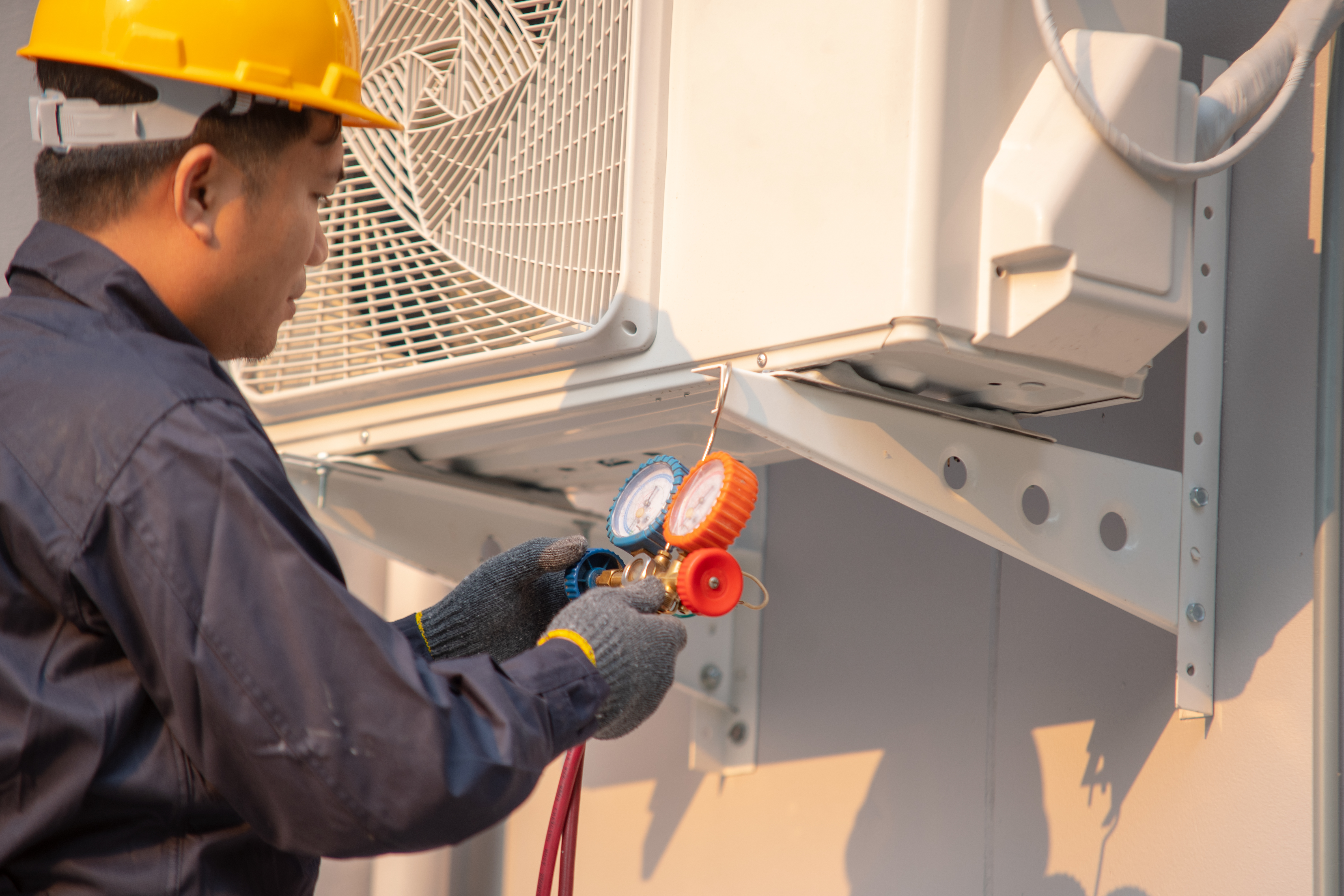 HVAC technician checking an outdoor air conditioning unit with manifold gauges