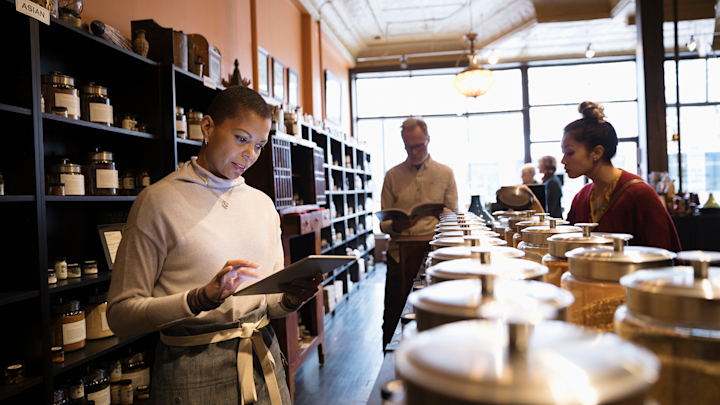 A person types at a tablet behind a counter at a coffee shop.