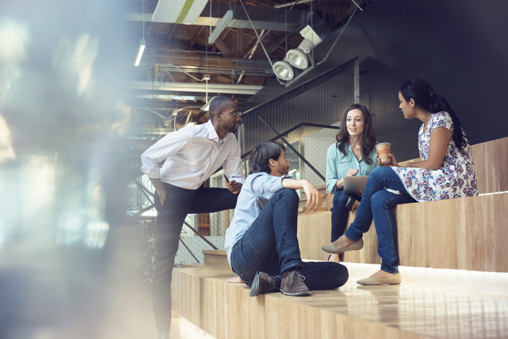 A group of four employees chats in an office while sitting and standing.