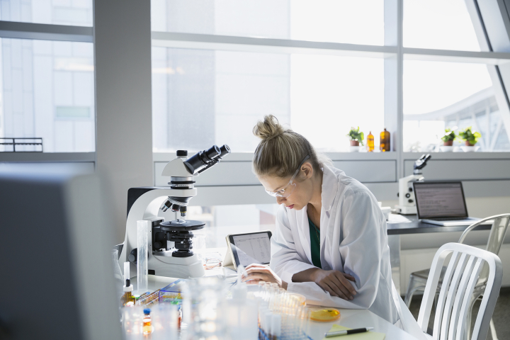 A person in a lab setting performs analysis with a microscope nearby.