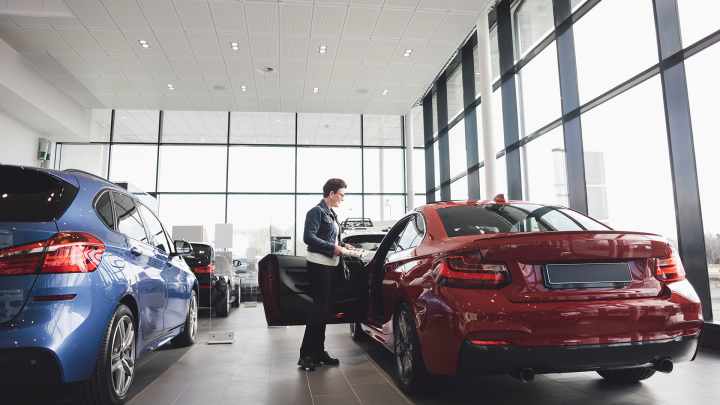 A person looks inside a red car in a showroom of new cars.