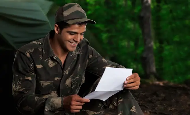 Military personnel reading a letter received in a care package with a smile on his face Military personnel reading a letter received in a care package with a smile on his face