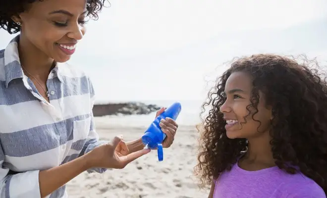 Mother applies sunscreen on her daughter to protect her daughter's skin