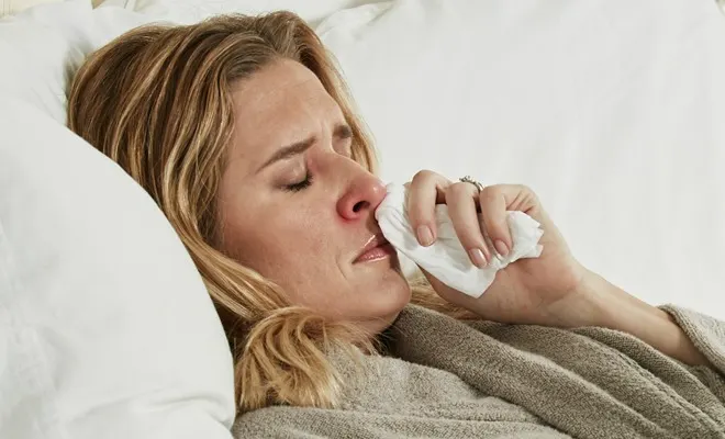 Woman sick in bed rubbing nose with a Puffs tissue