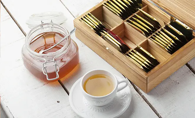 A cup of hot tea, honey, and tea packets to include for comfort in care package