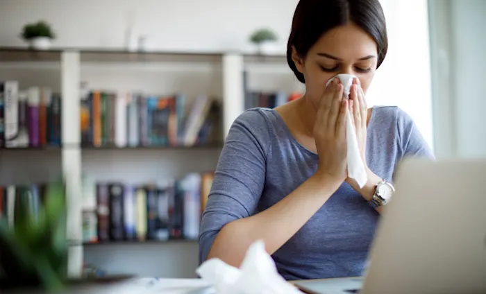 Woman blowing her nose at her computer
