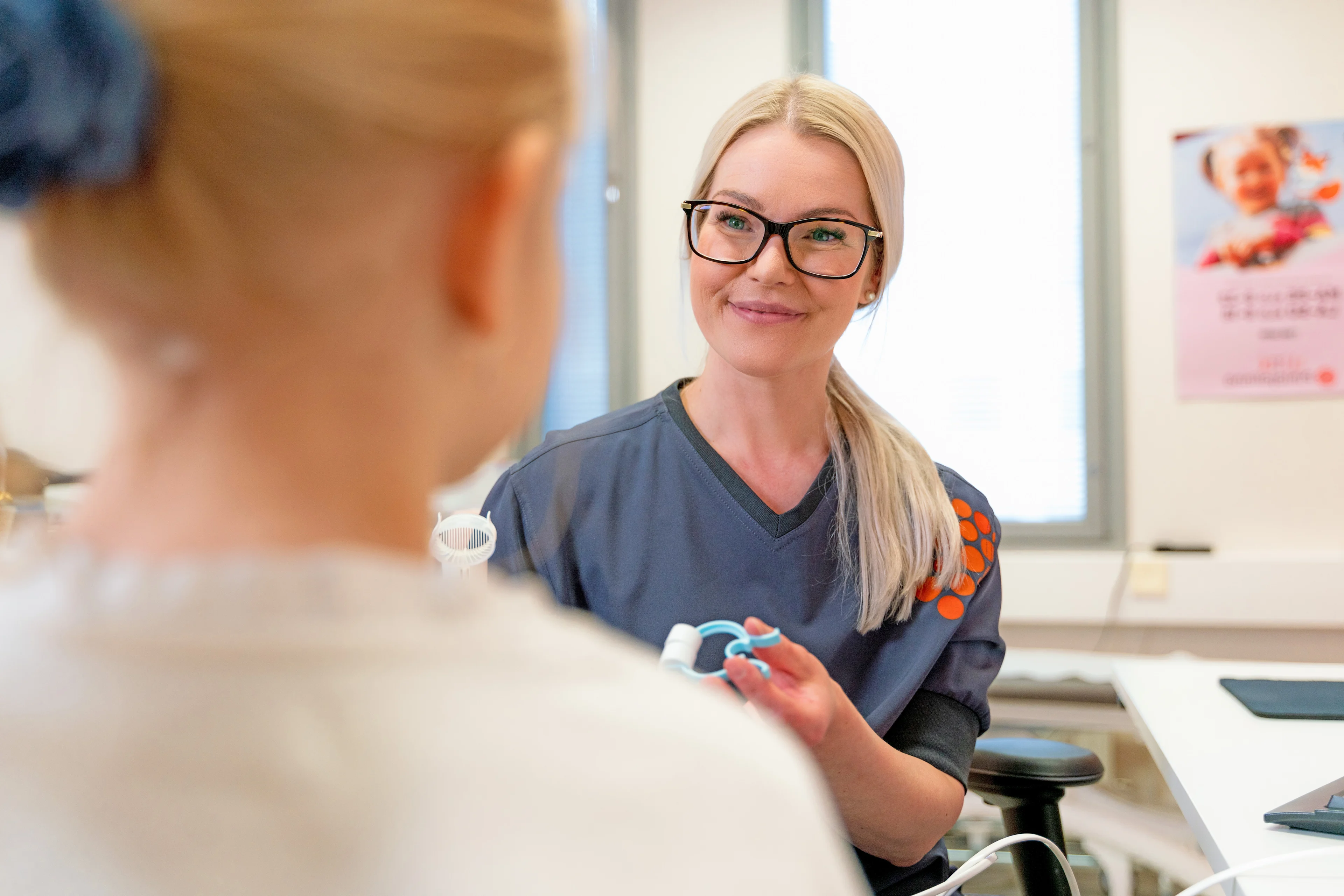 Vaaleatukkainen sairaanhoitaja hymyilee lapsipotilaalle terveydenhuollon vastaanotolla.