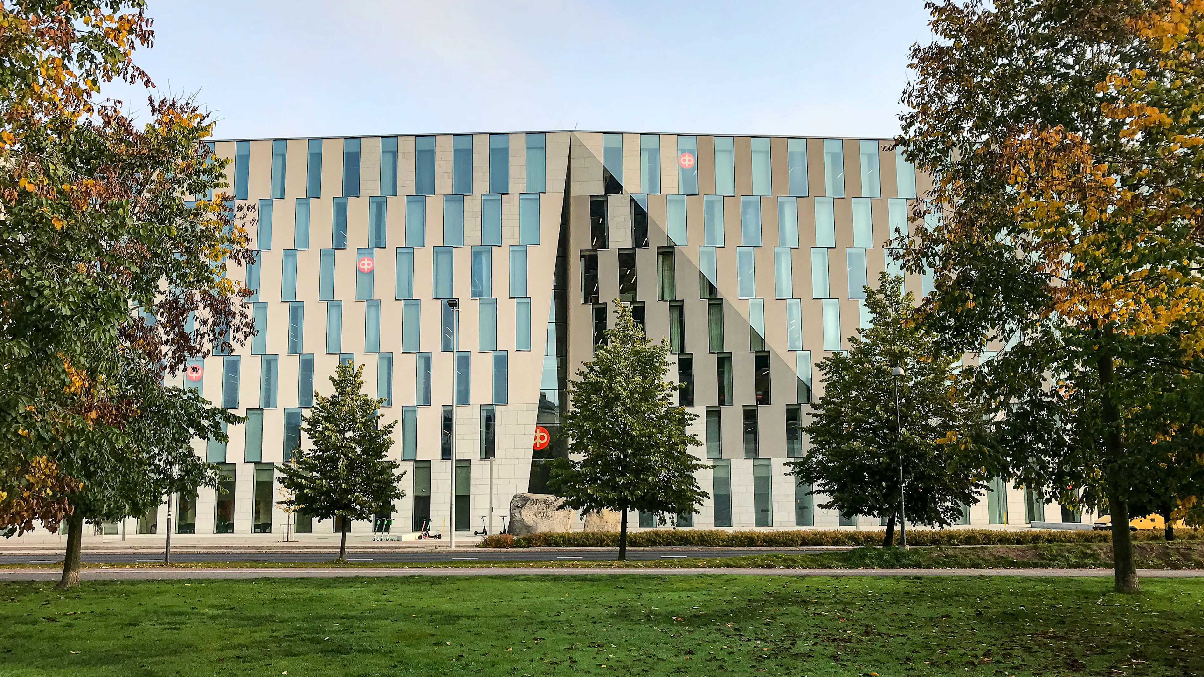 OP Vallilan julkisivu edestäpäin. Modernin rakennuksen edessä on puistomainen alue, jossa on vihreä nurmikko ja lehtipuita.