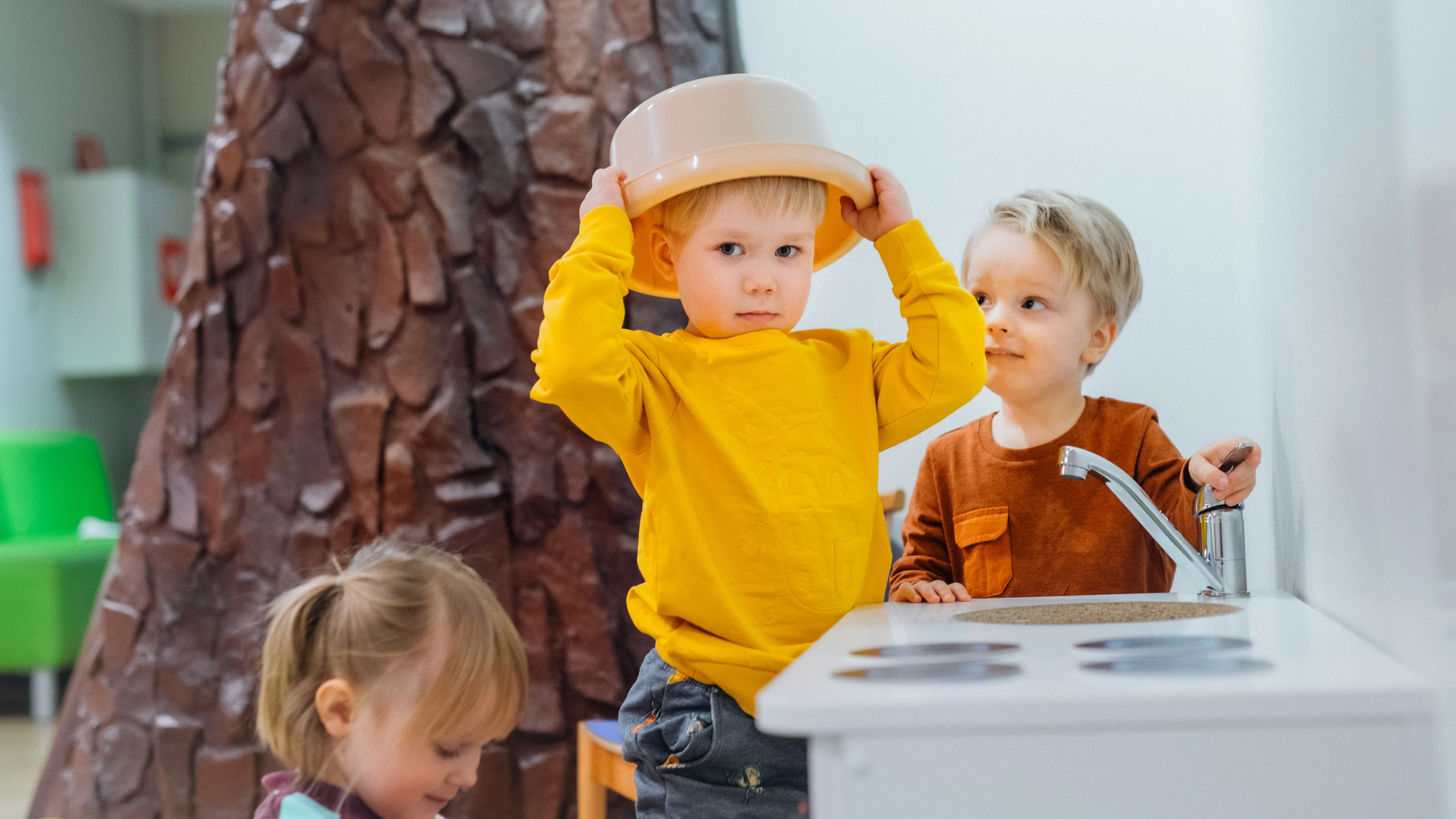 Kolme pikkulasta leikkii leikkikeittiön luona.