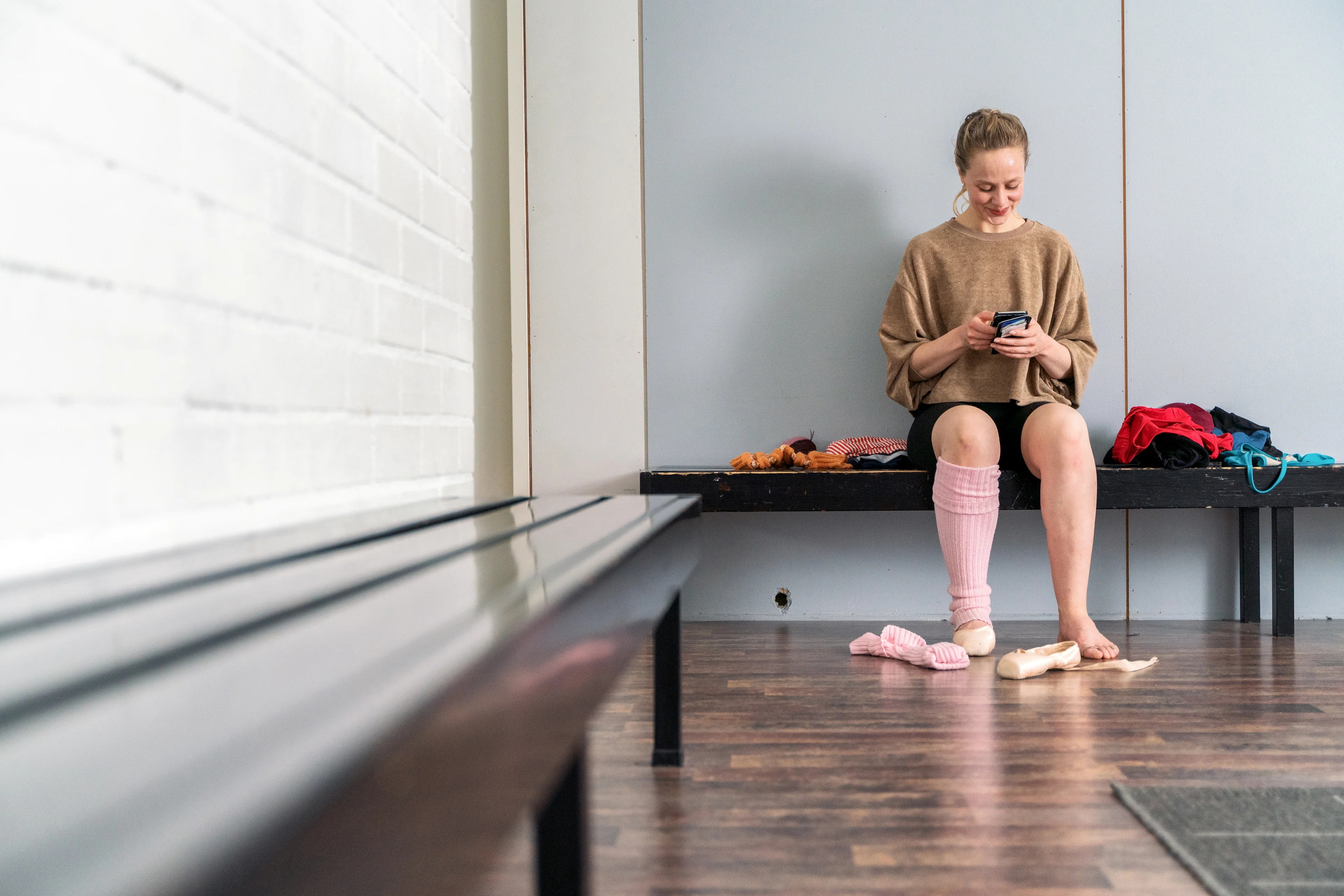 Ballerina istuu penkillä ja selaa puhelinta.