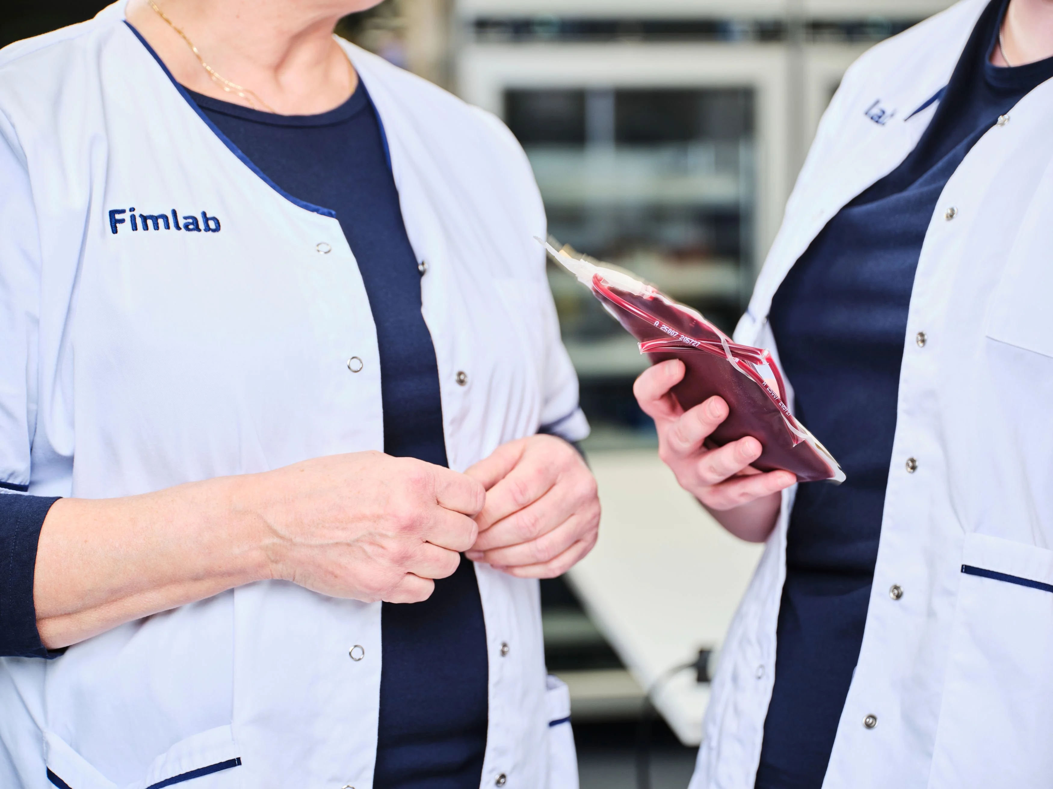 Kaksi henkilöä valkoiset takit päällä. Fimlabin logo rinnassa.