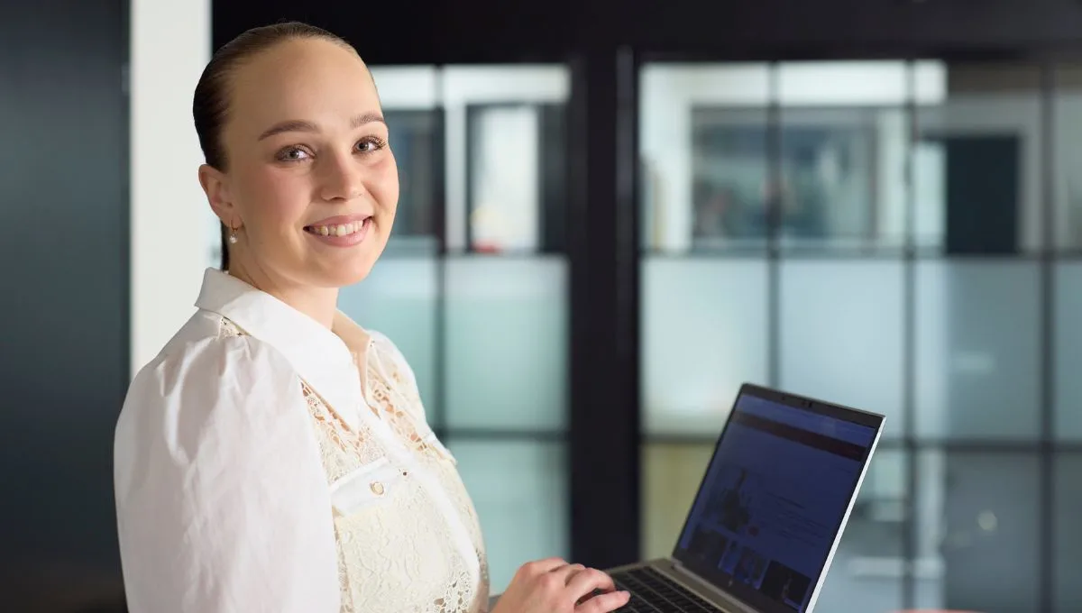 Hymyilevä nainen pitämässä kannettavaa tietokonetta modernissa toimistossa.