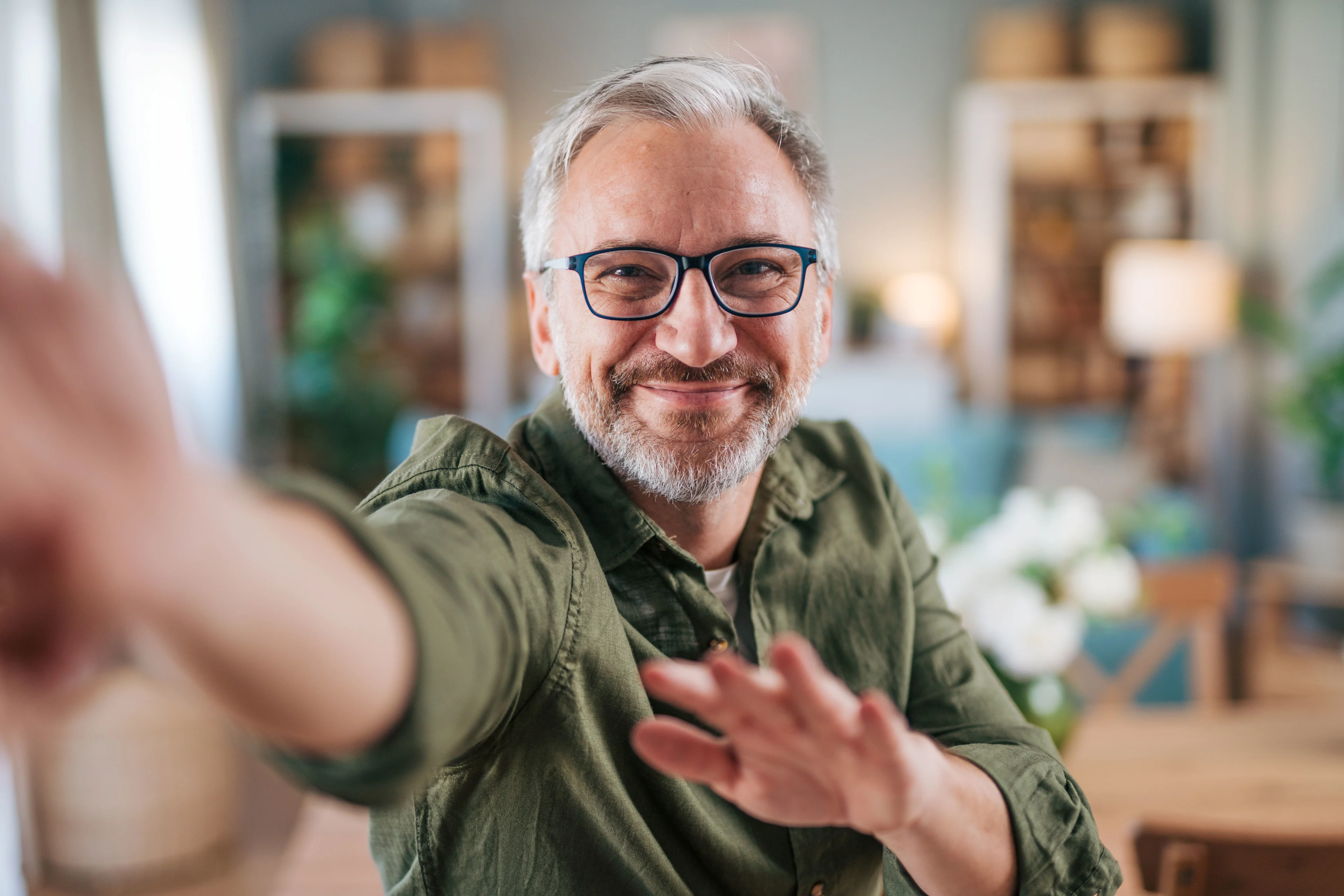Vihreäpaitainen vanhempi mies on kodikkaassa huoneessa ja ojentaa käsiään kohti.