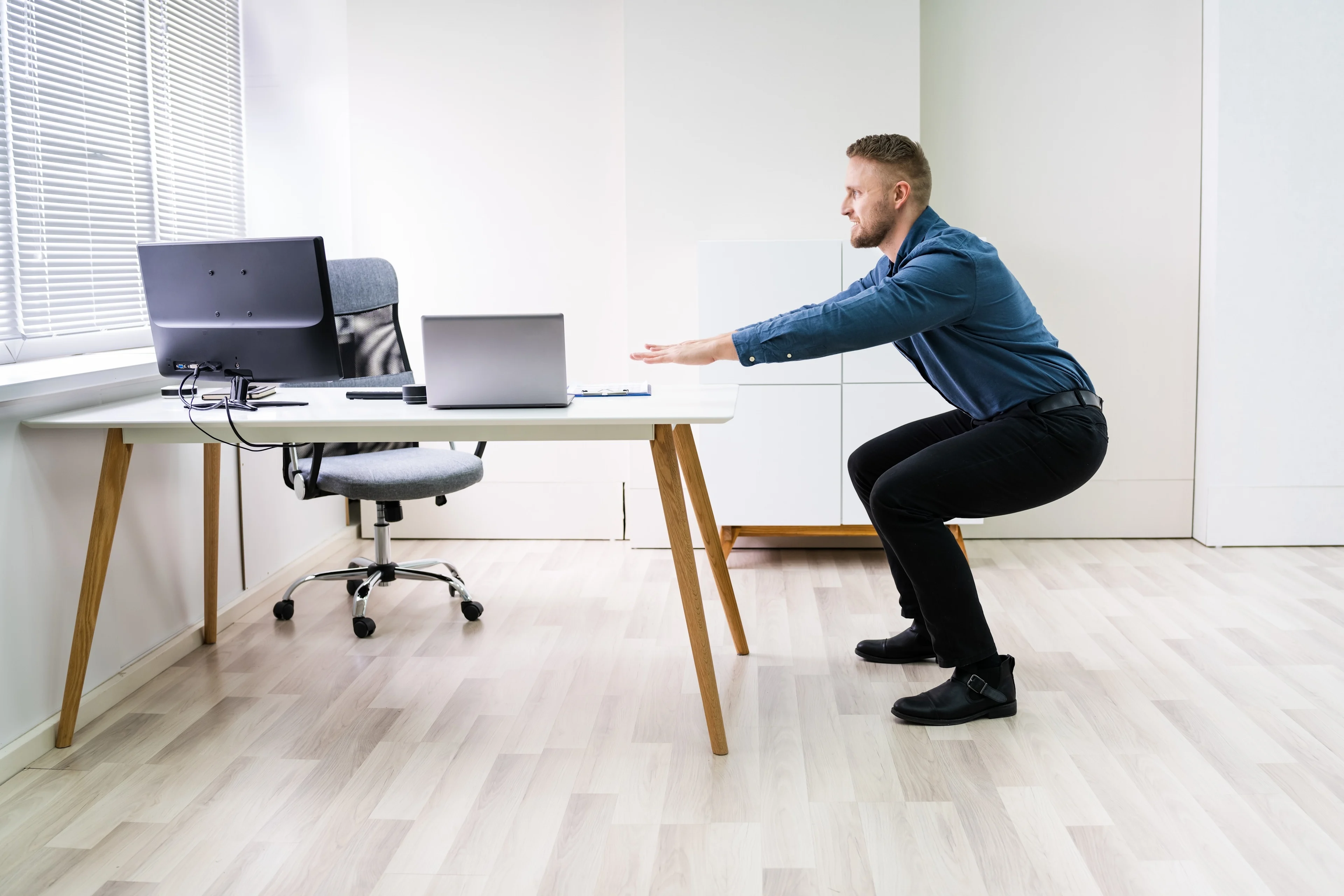 Mies tekee kyykkyjä työpöydän vieressä toimistossa taukojumpan aikana.