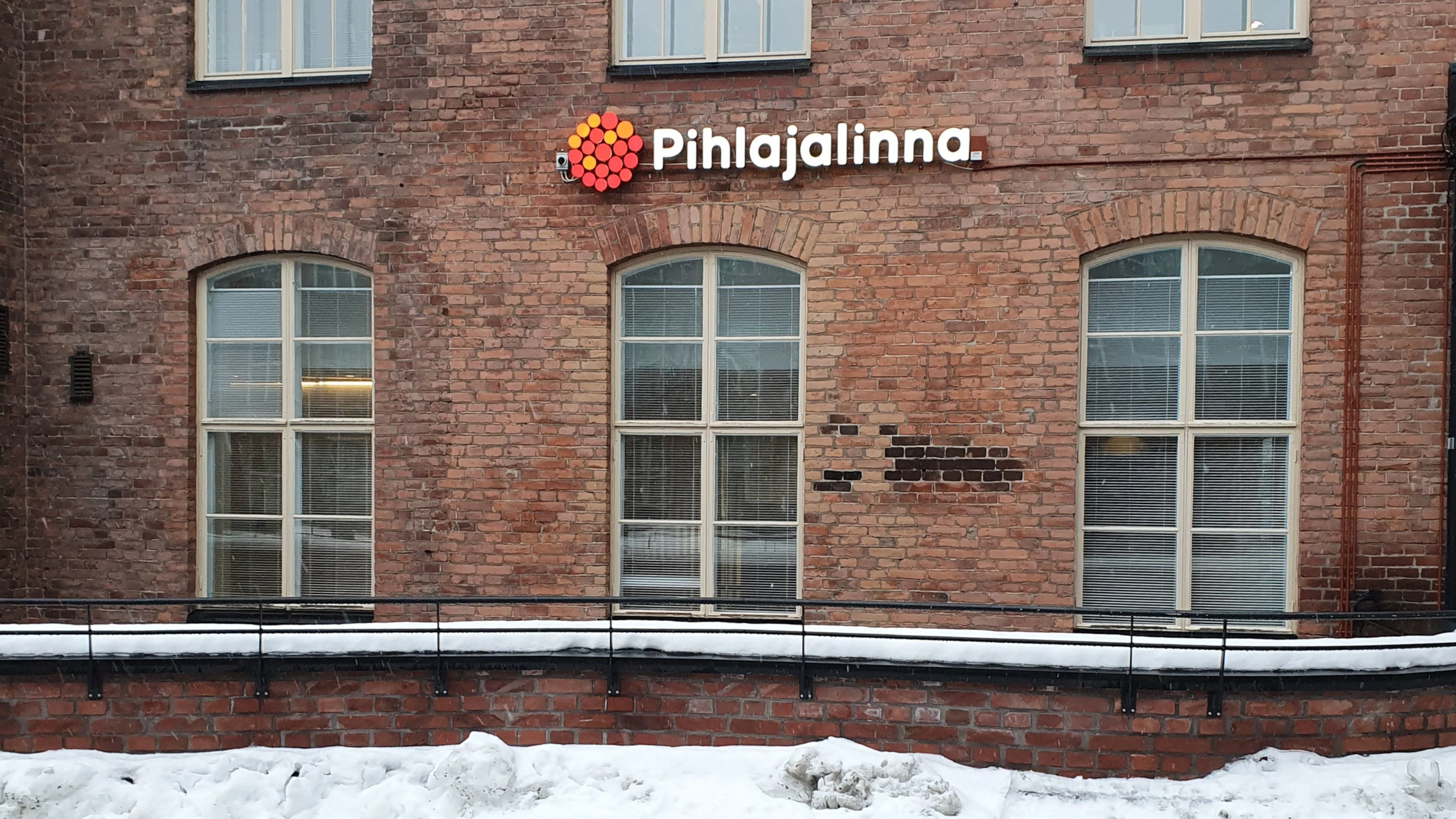 Tiiliseinää, jossa isoja korkeita ikkunoita sekä Pihlajalinnan logo seinällä