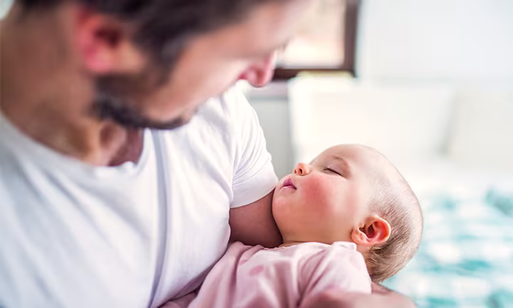 Dad and newborn bonding as a smiling father holds his baby close to his chest, both appearing relaxed and content in a warm home environment.