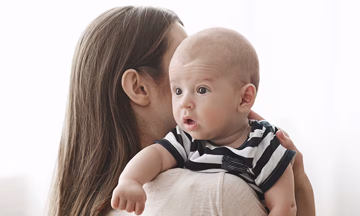 Baby in a striped onesie resting on parent's shoulder.