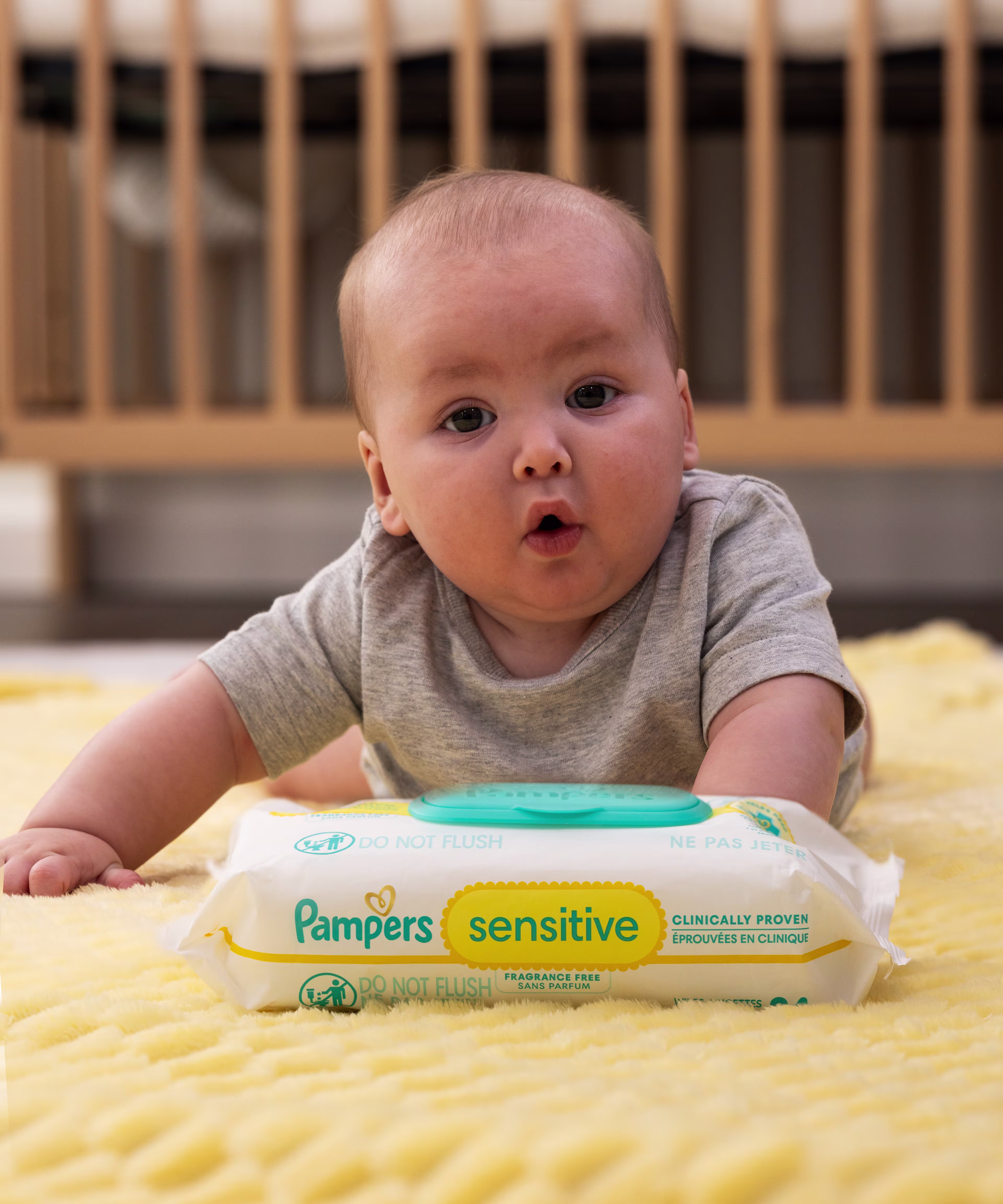 Baby on their tummy facing a pack of Pampers sensitive wipes with an adorable expression on their face.