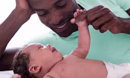 Father gently holding baby's hand, both smiling.