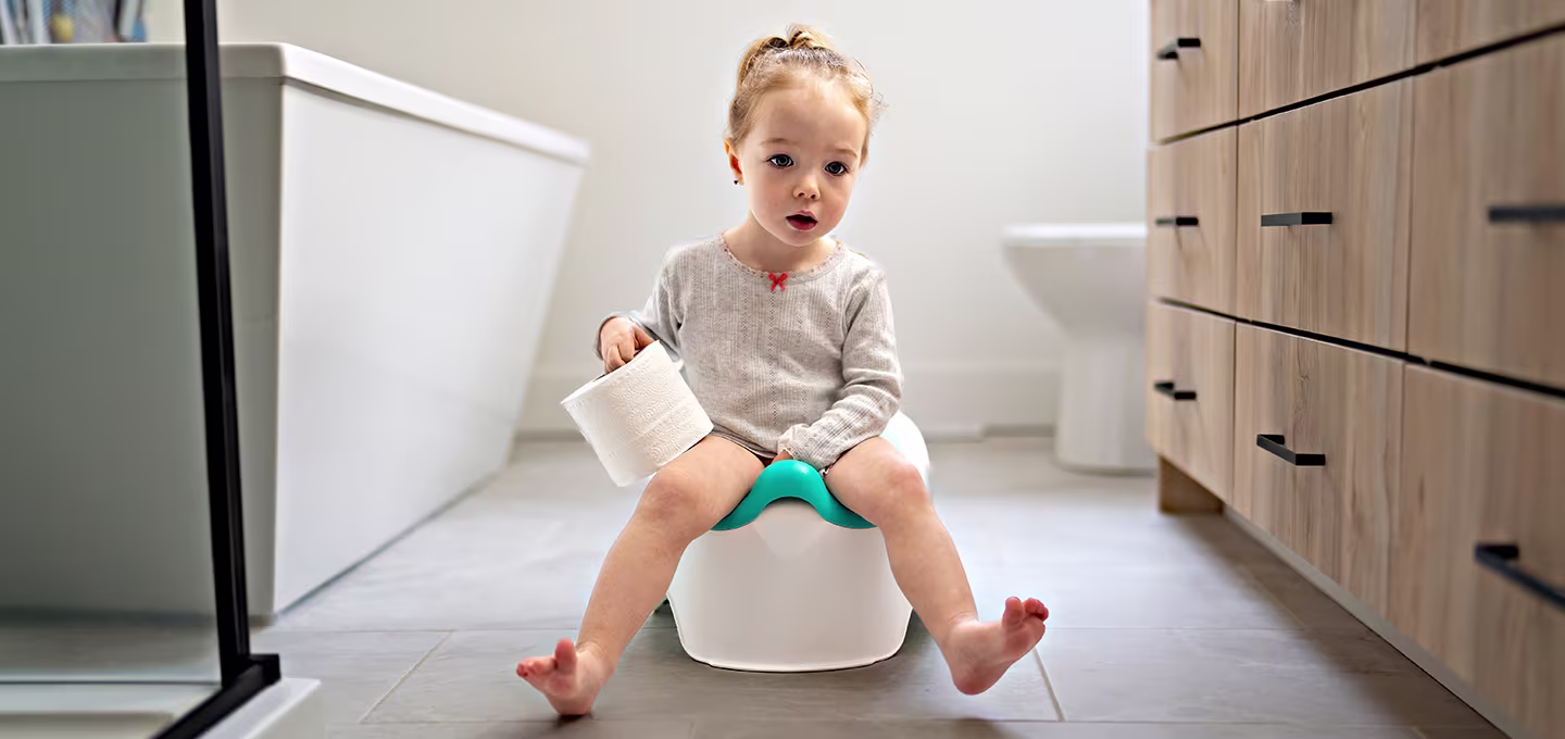 A toddler sitting on the potty, holding a roll of toilet paper