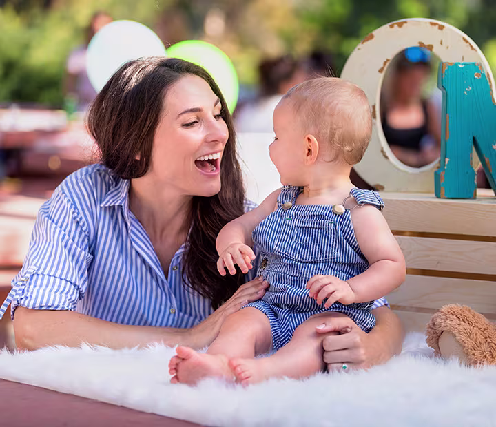 Mother and baby in matching striped outfits sharing a joyful moment outdoors, sitting on a soft blanket.