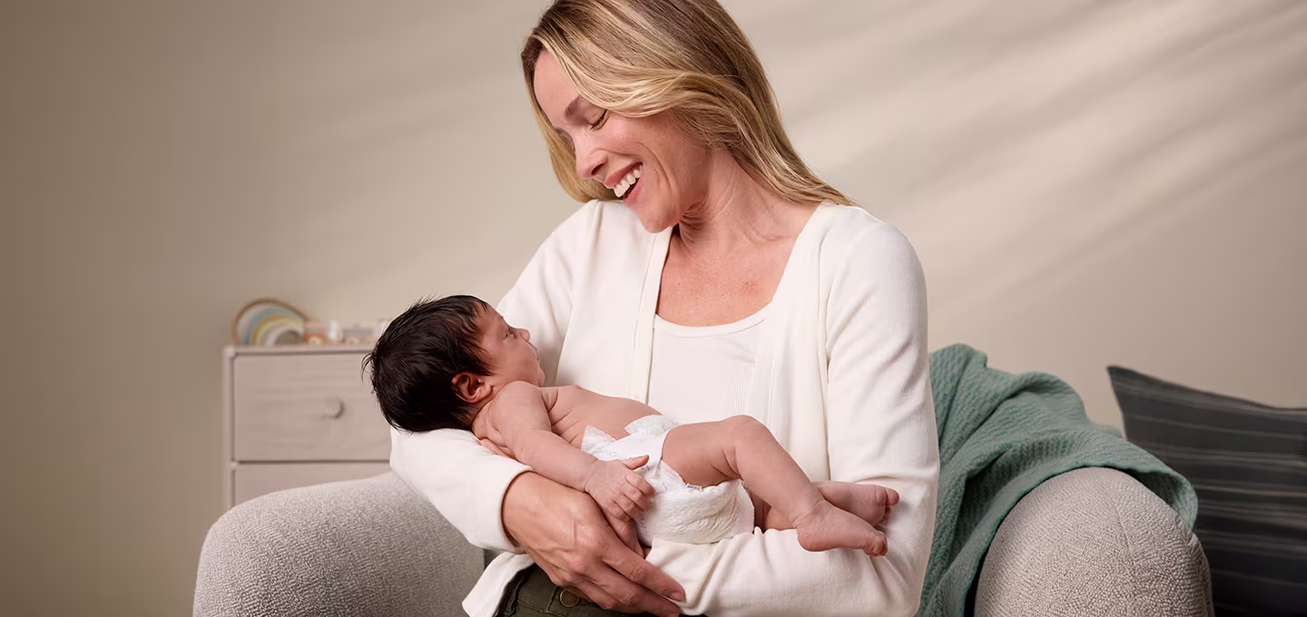 Smiling parent holding a newborn baby on a sofa, showing a calm, nurturing moment.