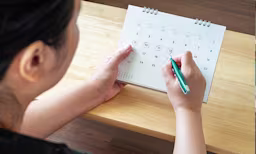 A person circling dates on a calendar/planner to track menstrual cycle