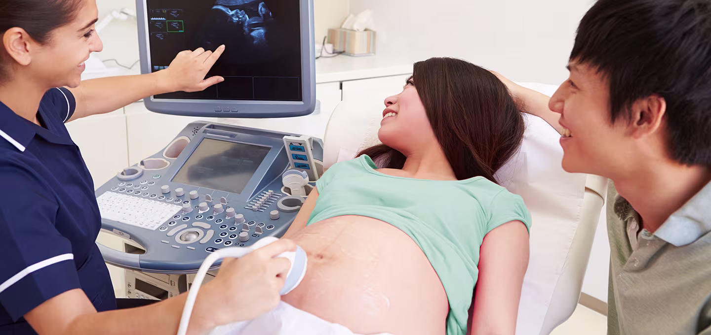 Smiling couple watching ultrasound with technician in a clinic.
