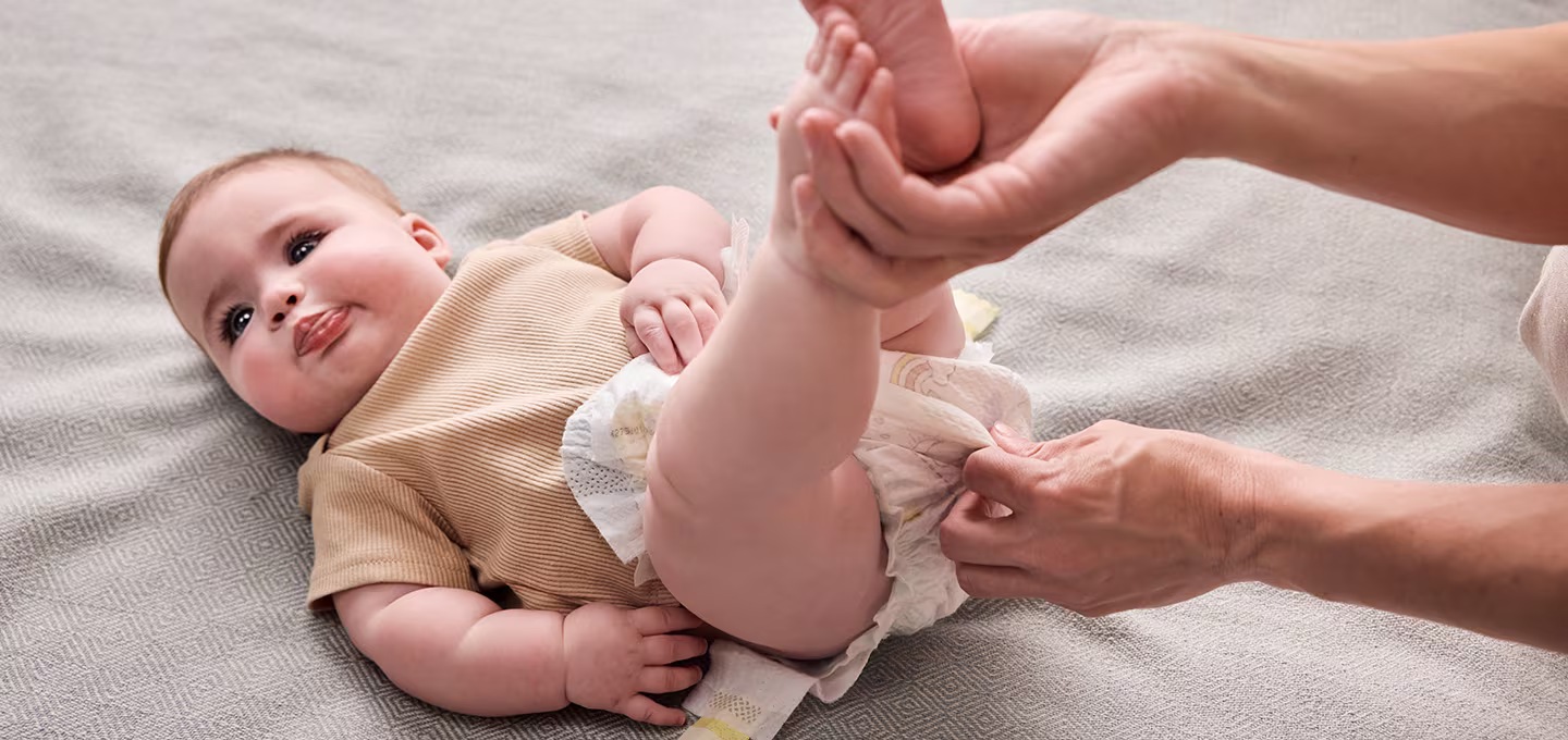 An adult’s hands gently fastening a clean diaper on a lying baby during a diaper change, showing proper placement and technique