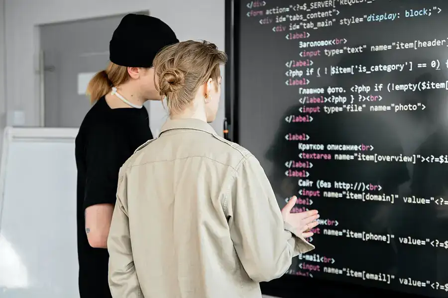 a man and woman on the web development team analyze a series of code on a big screen