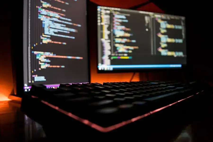 a close up shot of a red-lit keyboard and two monitors displaying web development code. 