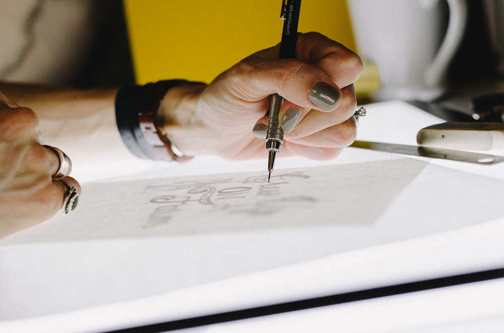 a close up image of a woman's hand sketching a design on paper